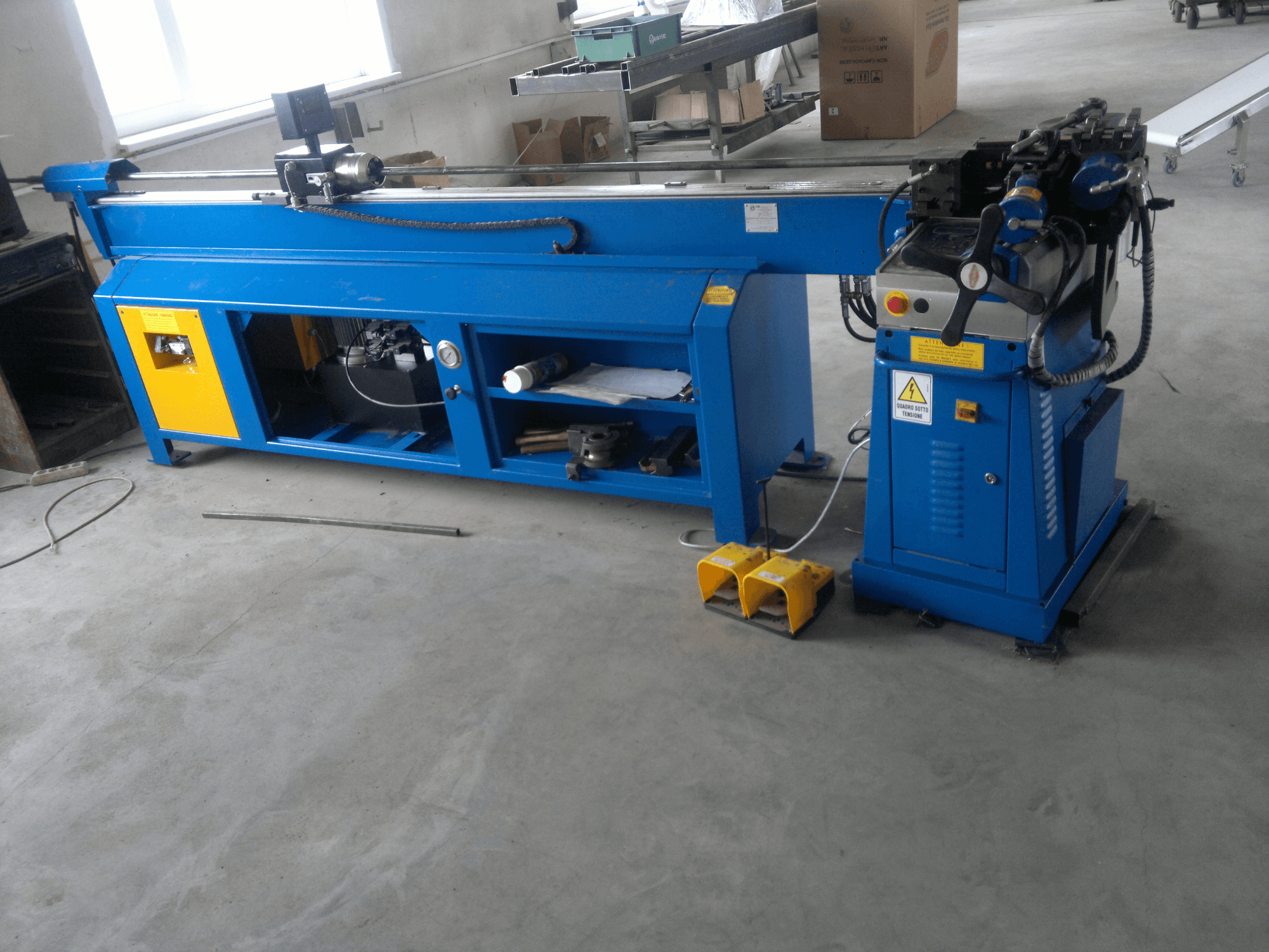 Máquina para trabalhar madeira azul com detalhes em amarelo, vista lateral; possui painel de controlo, pedais e um conjunto de lâminas rotativas.