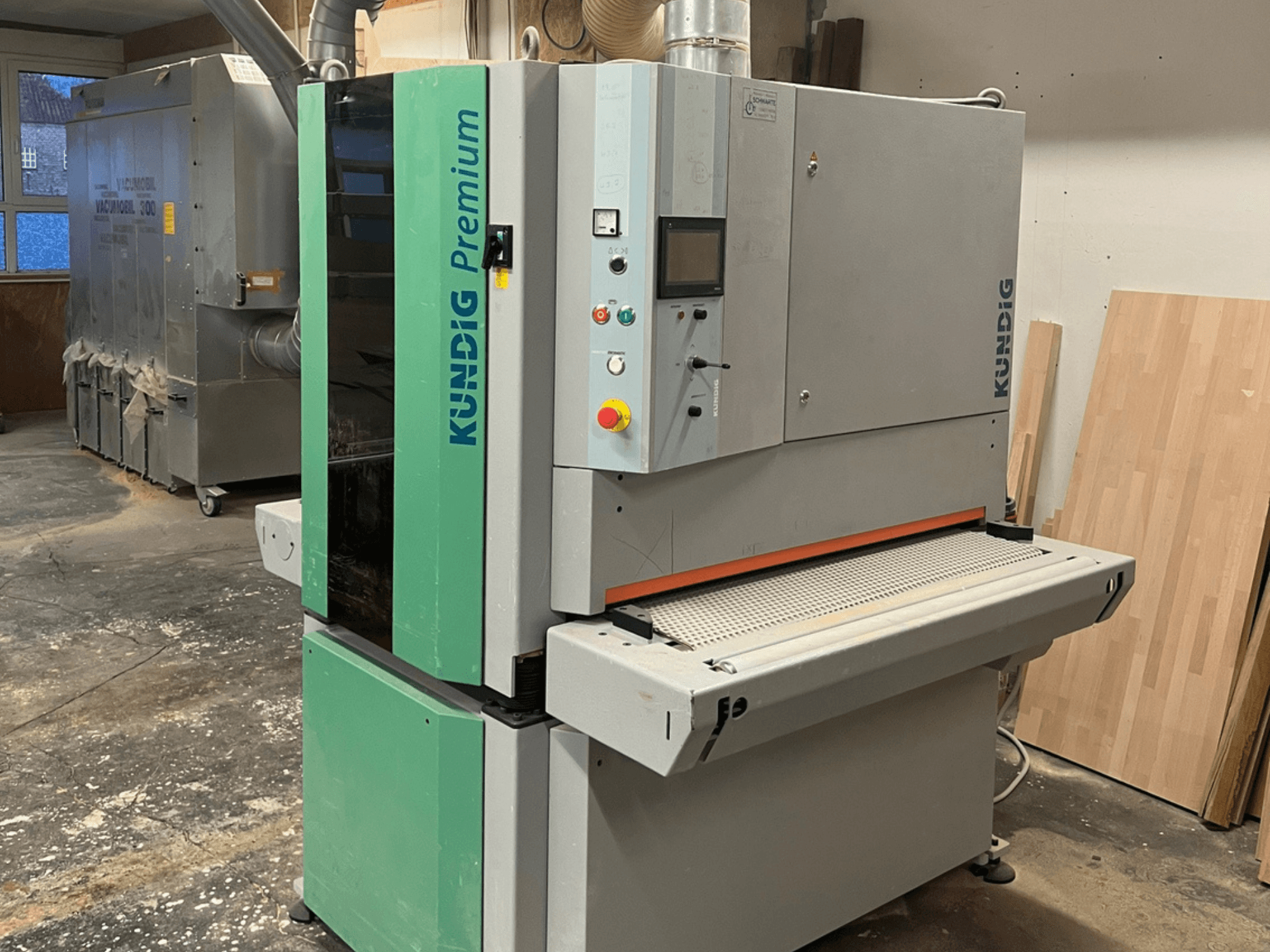 Lixadeira de cinta Kundig Premium-1 1100K em cinzento e verde, vista de lado com o painel de controlo e a cinta de lixa visíveis.