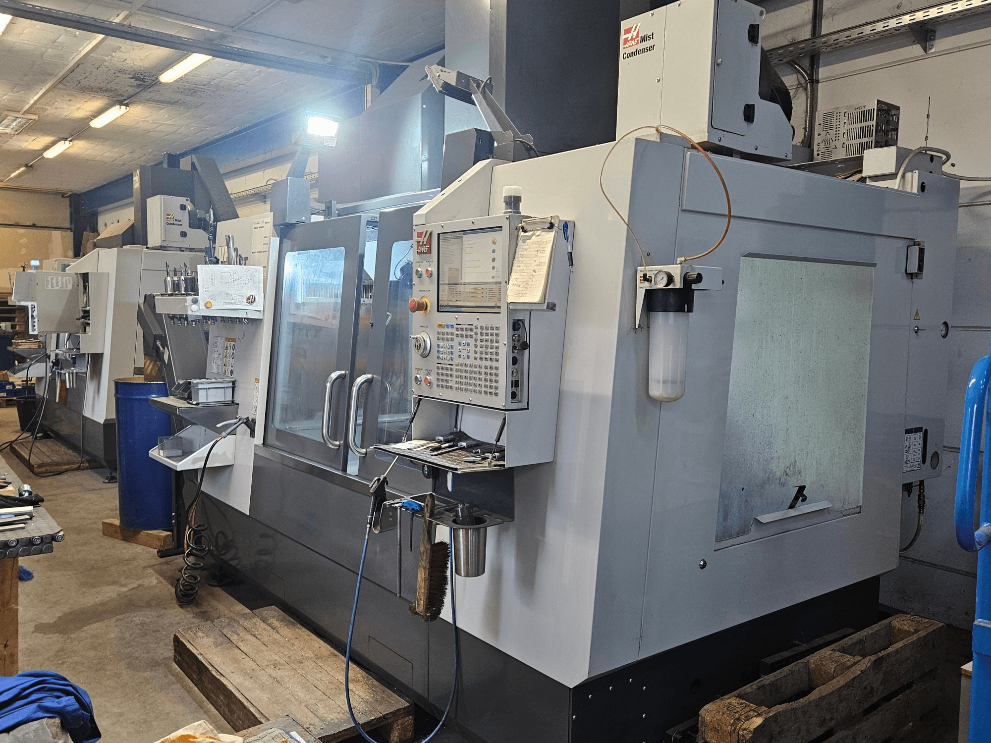 Centro de maquinagem vertical Haas VF-3YT/50 numa oficina, vista frontal que mostra o painel de controlo, os porta-ferramentas e o condensador de névoa.