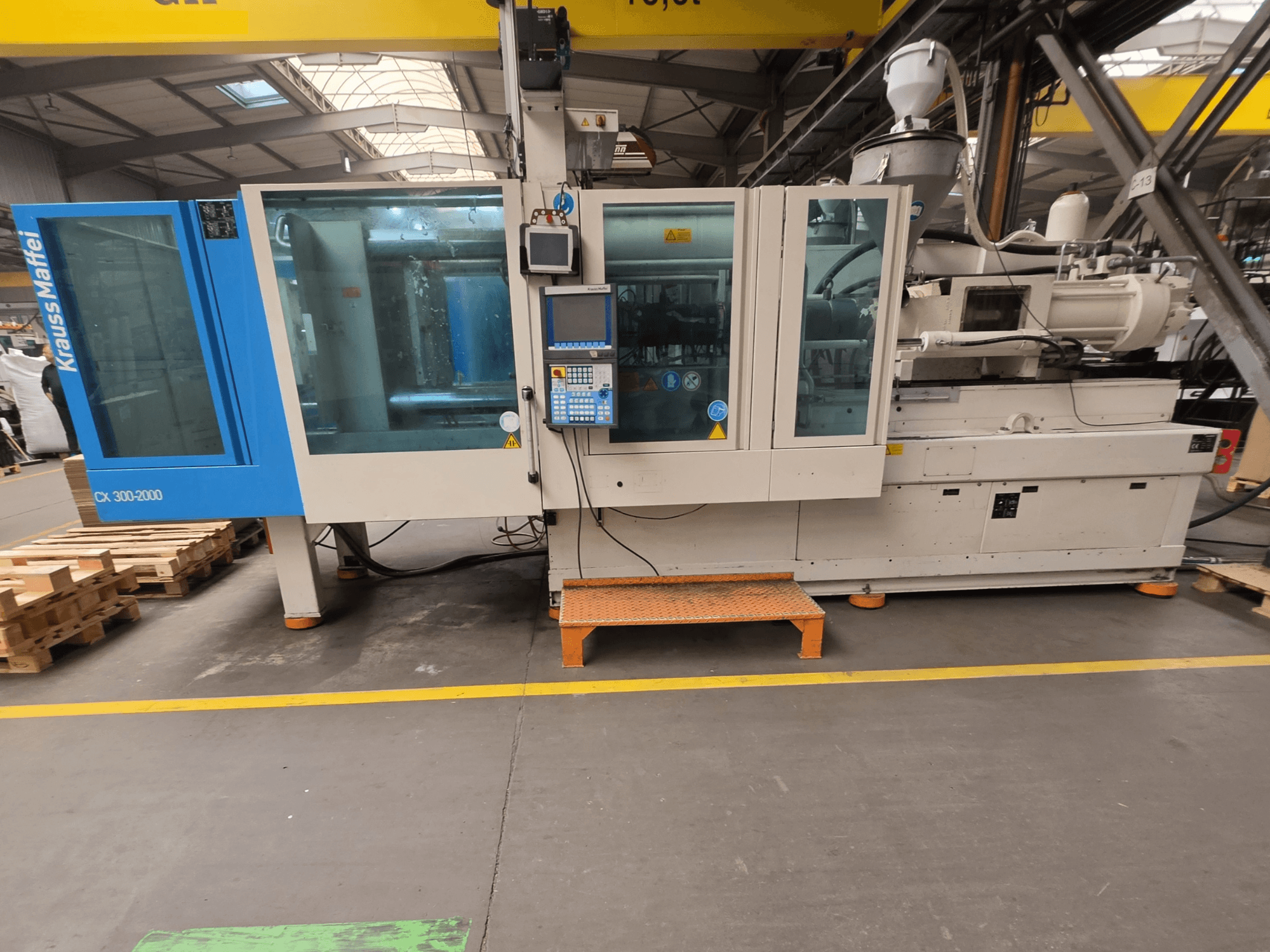 Máquina de moldagem por injeção hidráulica Krauss Maffei 300-2000 CX, vista lateral mostrando o painel de controlo e as grandes janelas.