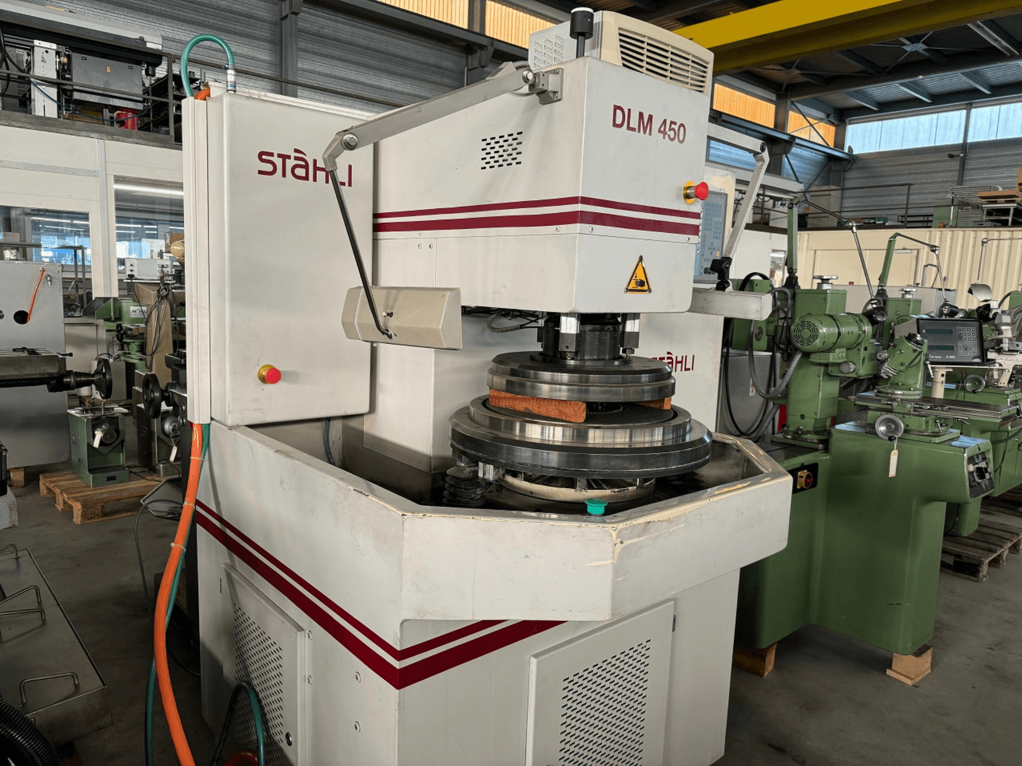 Máquina de retificação plana STAEHLI DLM 450, vista frontal com disco de retificação e painel de controlo, num ambiente industrial.