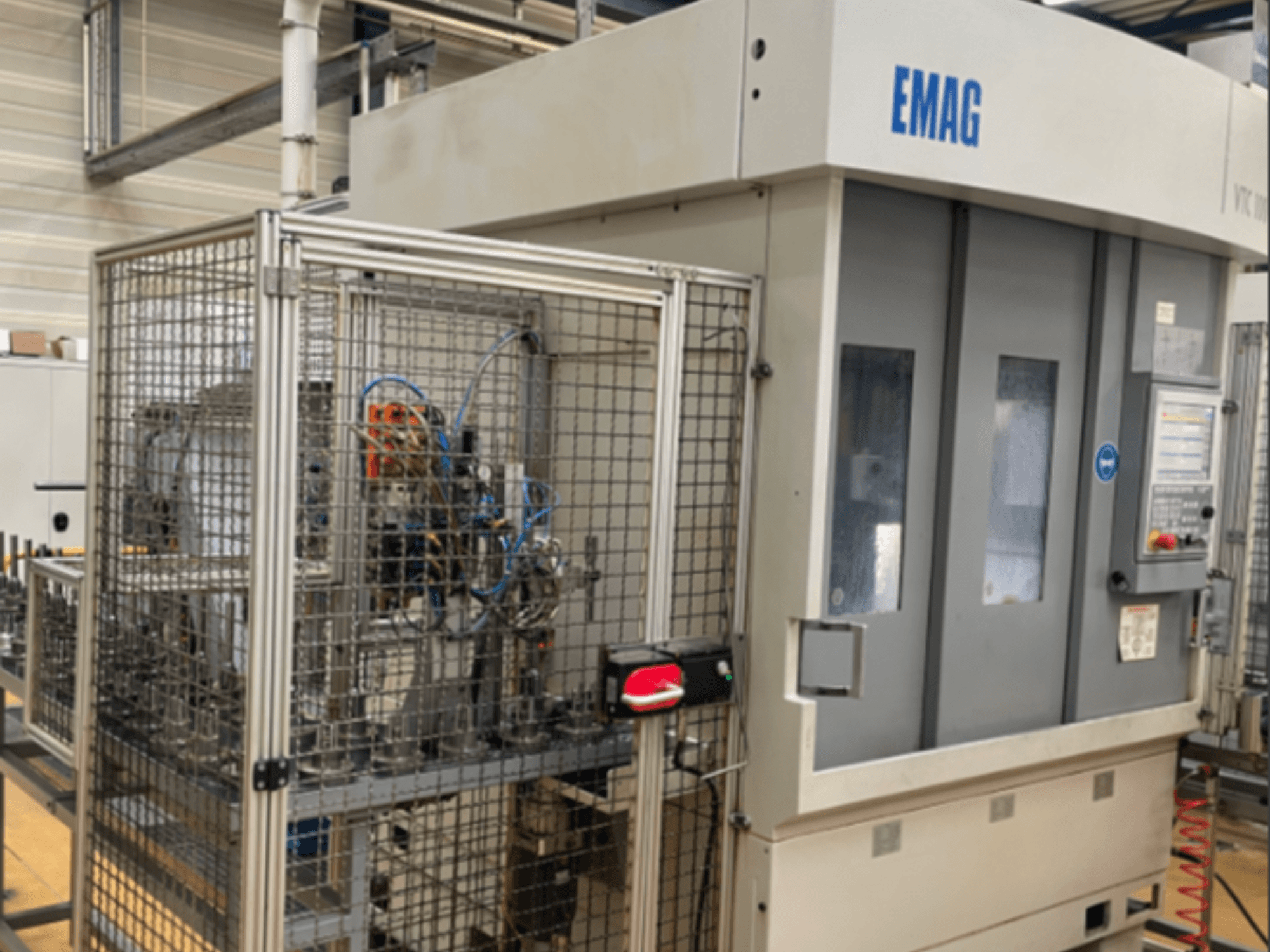 Torno vertical EMAG VTC 100 visto de lado, mostrando o painel de controlo e os detalhes da barreira de segurança.