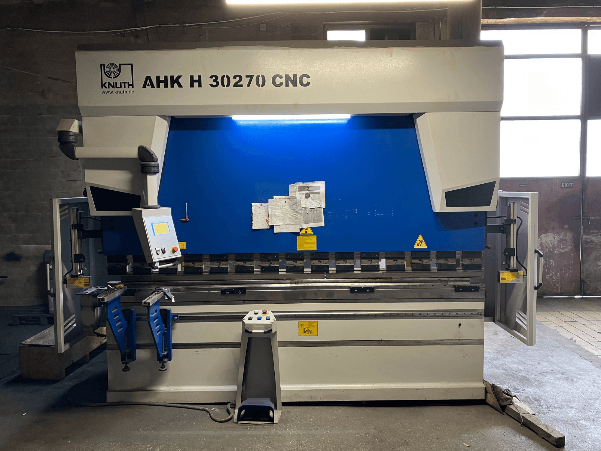 Prensa-dobra CNC KNUTH AHK H 30270 numa oficina, vista frontal, mostrando o painel de controlo e o design azul/branco, com a porta lateral aberta.