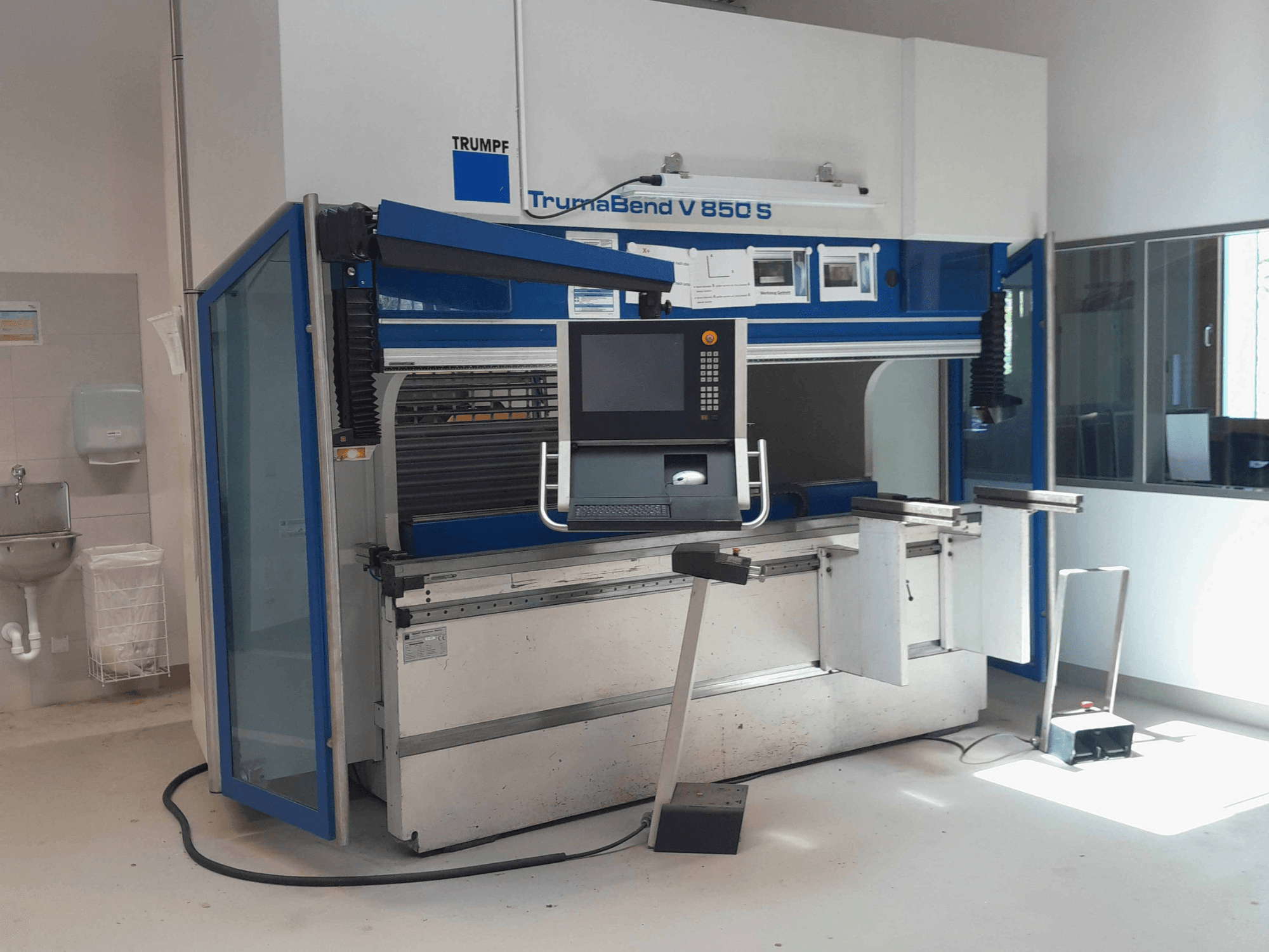 Prensa-dobra TRUMPF TrumaBend V 850 S, vista frontal com painel de controlo e dispositivos de segurança num espaço de trabalho bem iluminado.