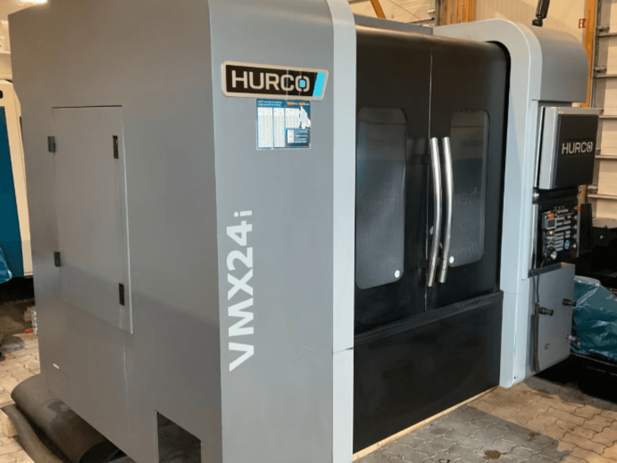 Centro de usinagem vertical Hurco VMX 24i, vista frontal com carroçaria cinzenta metálica, portas de painéis pretas e interface de controlo.