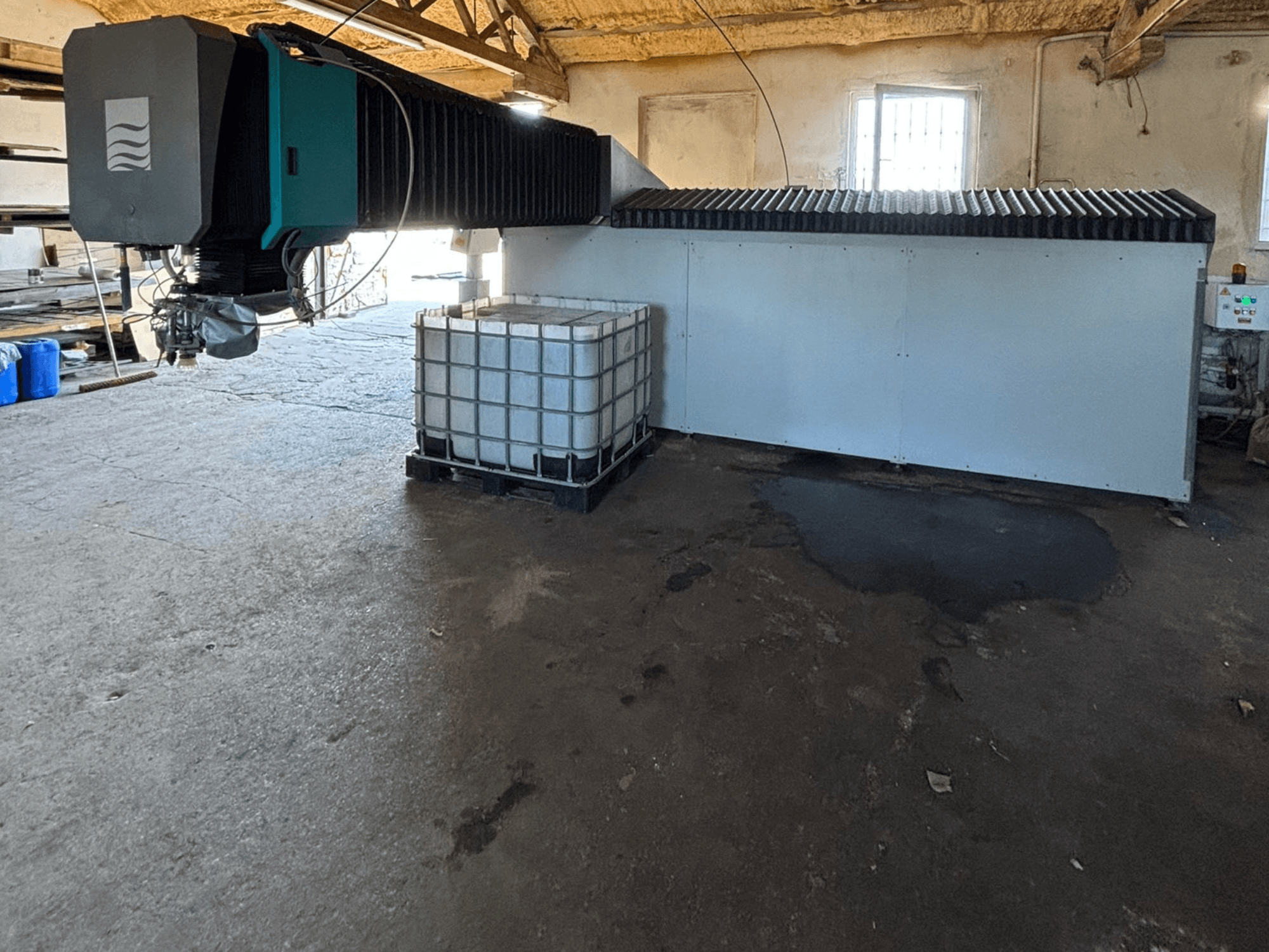 Máquina industrial de jato de água numa oficina, vista lateral, com um grande depósito de água e um painel de controlo visível ao lado.