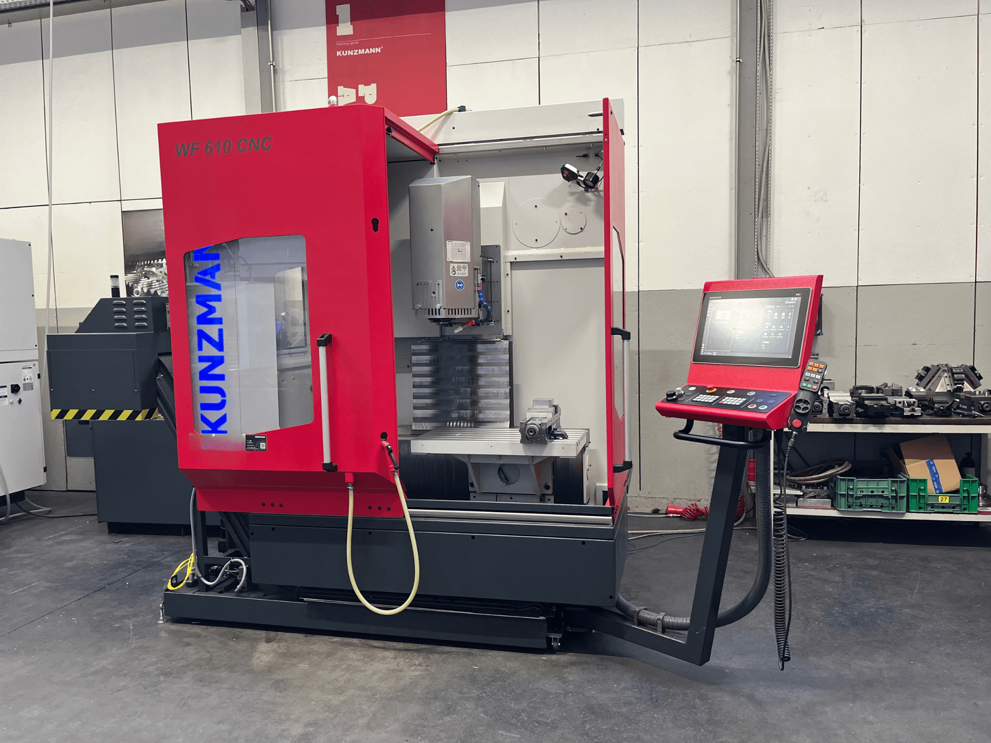 Centro de maquinagem vertical CNC KUNZMANN WF 610 numa oficina, com um painel de controlo e componentes da máquina visíveis.
