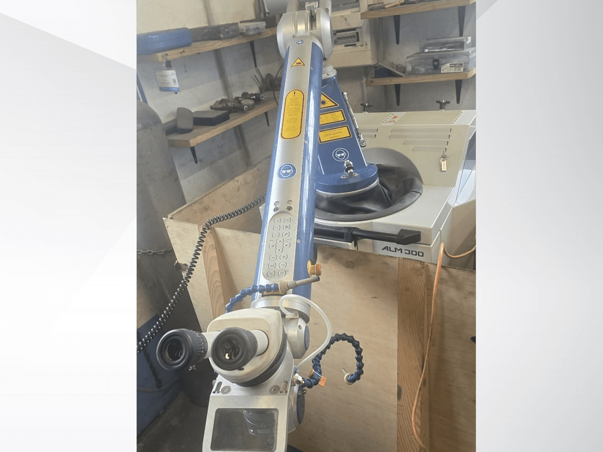 Vista frontal da máquina de soldadura a laser ALPHA LASER ALM 300, equipada com um braço robótico, lentes óticas e painel de controlo.