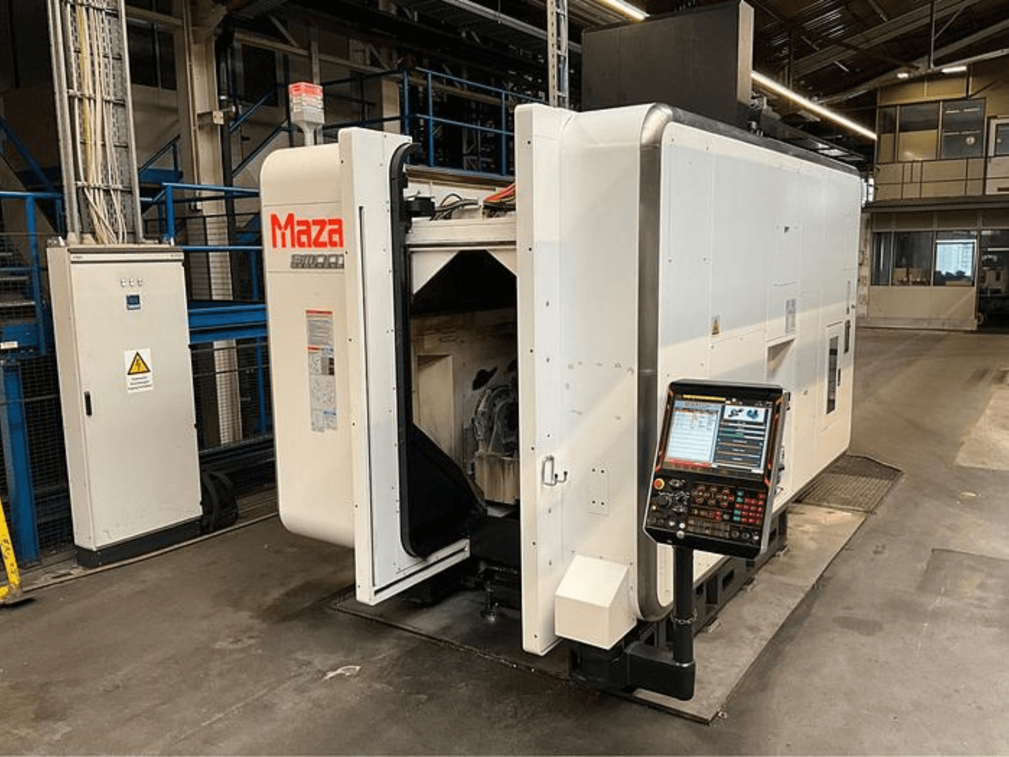 Máquina CNC Maza mostrada de frente, com painel de controlo, design industrial e componentes de máquinas visíveis.