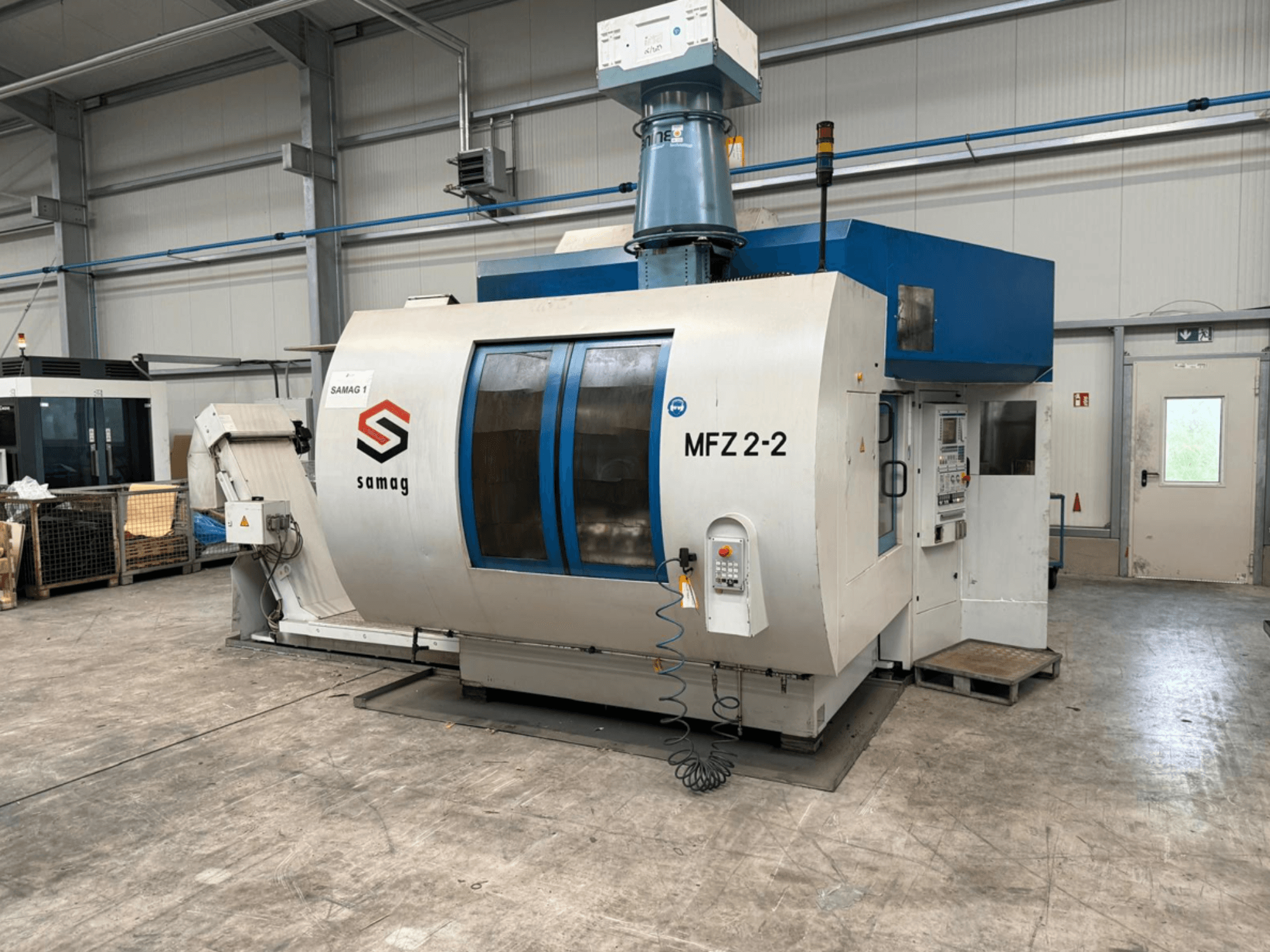 Máquina-ferramenta Samag MFZ 2-2, vista frontal, mostrando o painel de controlo e o tampo azul, com dispositivos de segurança num ambiente industrial.