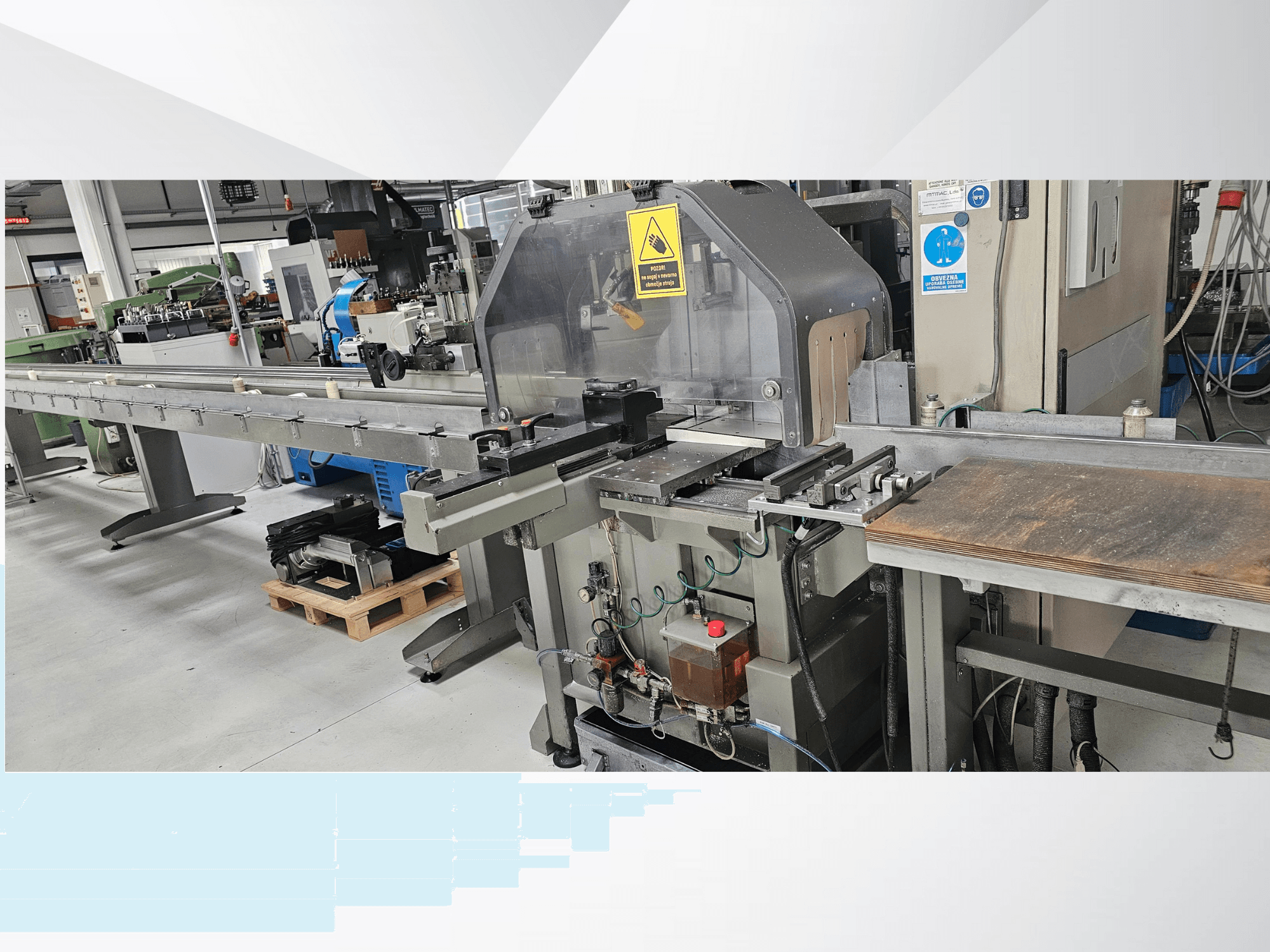 Máquina de corte industrial vista de lado, com um longo tapete rolante, painel de controlo e avisos de segurança.