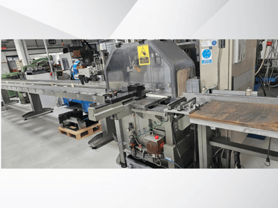 Máquina de corte industrial vista de lado, com um longo tapete rolante, painel de controlo e avisos de segurança.