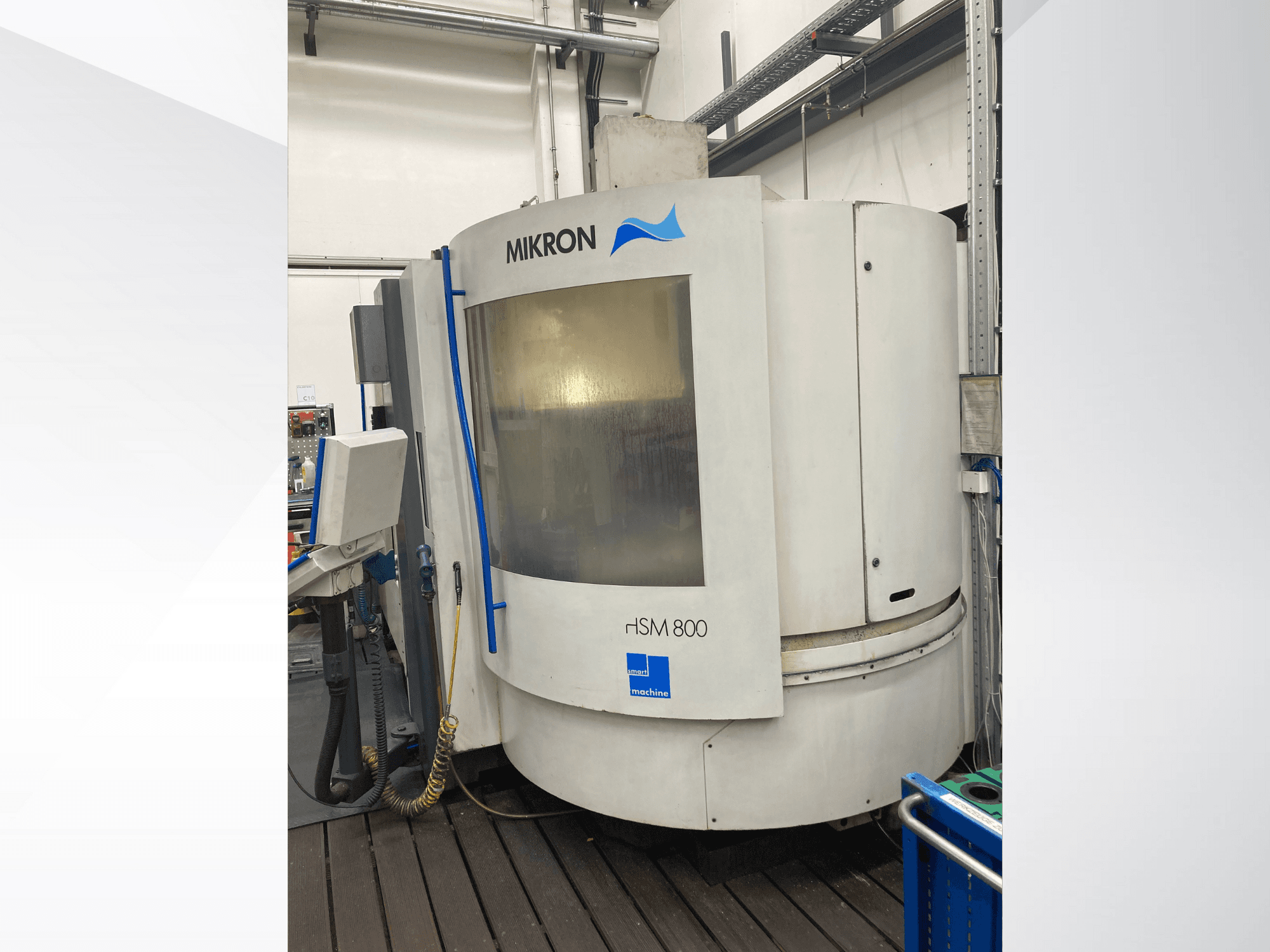 Máquina CNC Mikron rISM 800, vista frontal com painel de controlo, design cilíndrico e detalhes em azul, inserida num ambiente de oficina.