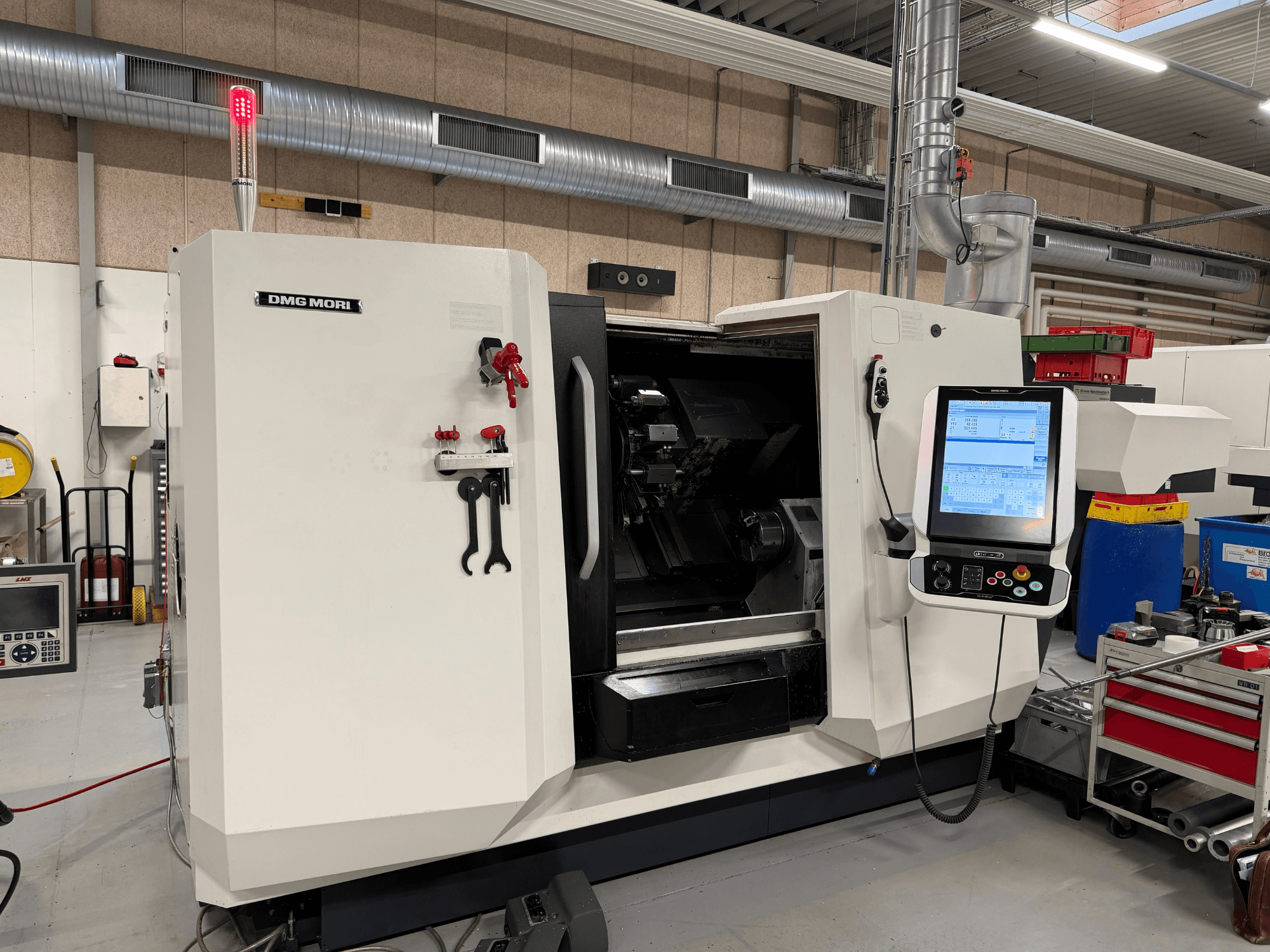 Torno horizontal DMG MORI CLX 450 V6, vista frontal com o painel de controlo, o botão de paragem de emergência e a luz de segurança visíveis.
