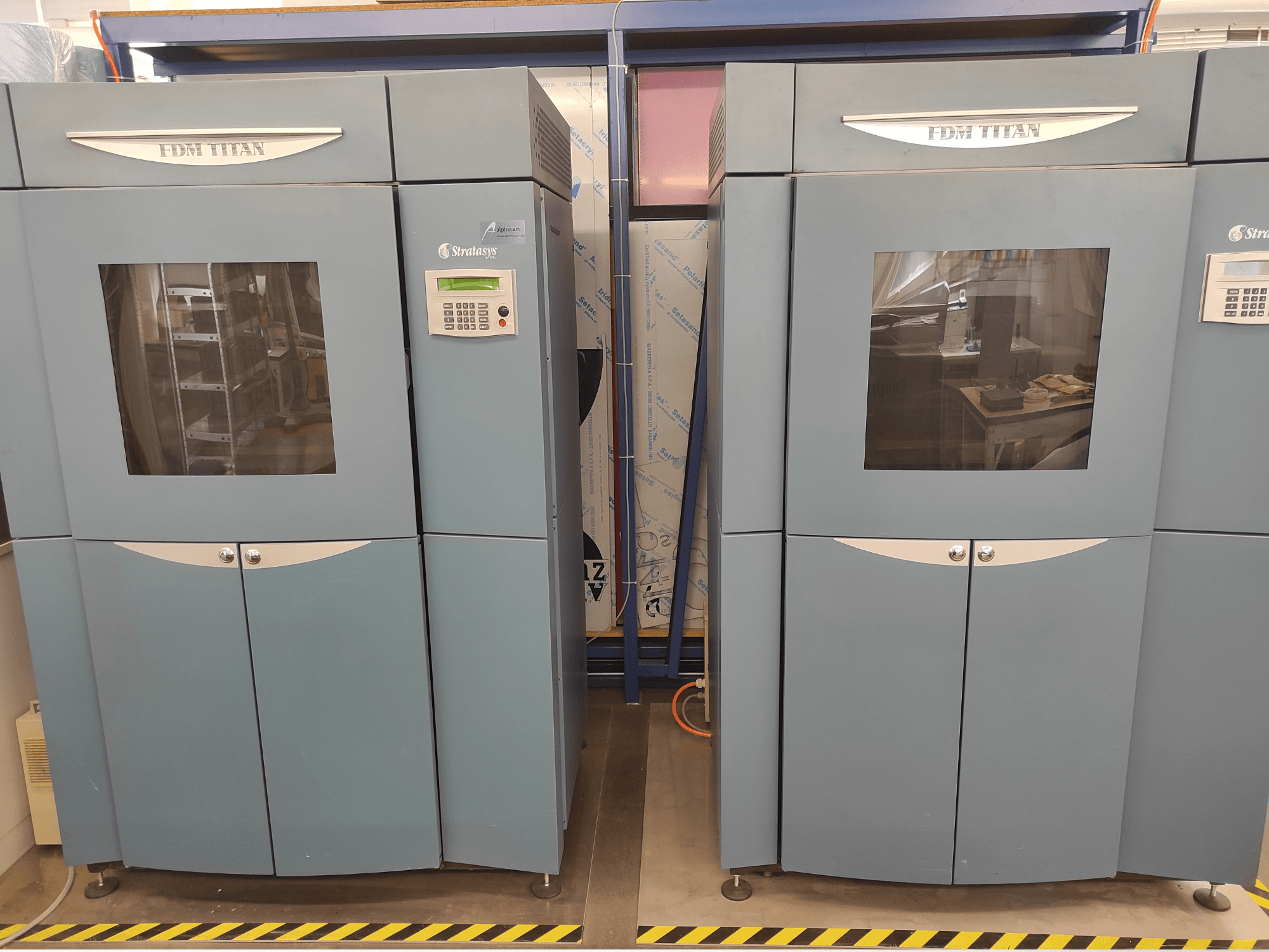 Vista frontal da impressora 3D de plástico Stratasys FDM TitanTI T0031; apresenta um painel de visualização e uma janela transparente.