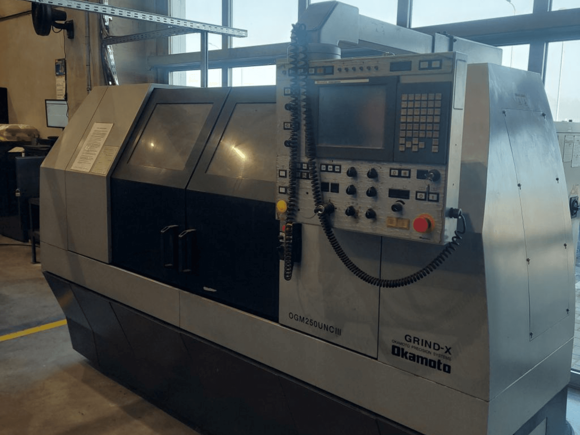 Máquina de retificação cilíndrica OKAMOTO OGM 250 UNC III, vista frontal, mostrando o painel de controlo e o design com janela dupla.