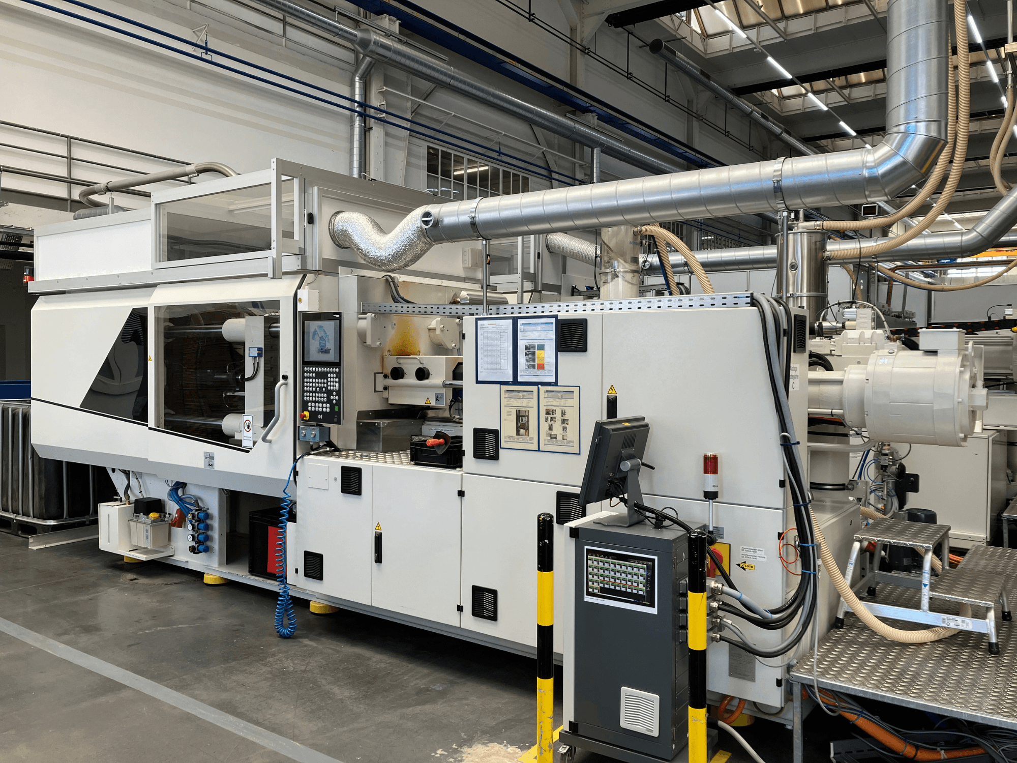 Vista frontal de uma máquina industrial com painel de controlo, tubos e ecrãs de visualização, com um design branco elegante e detalhes técnicos.