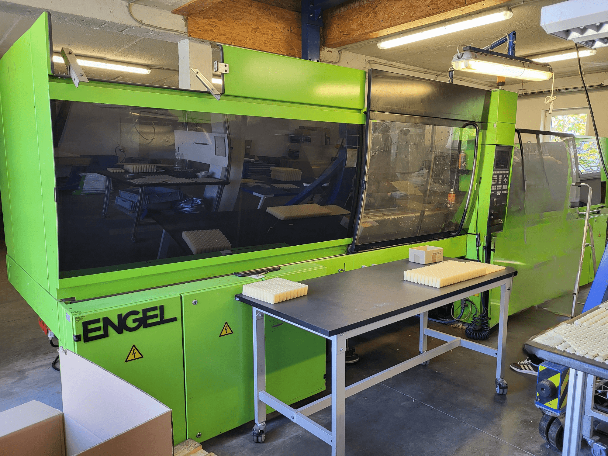 Máquina de moldagem por injeção hidráulica Green Engel ES1800/300HL vista de frente, com materiais empilhados numa mesa de trabalho.
