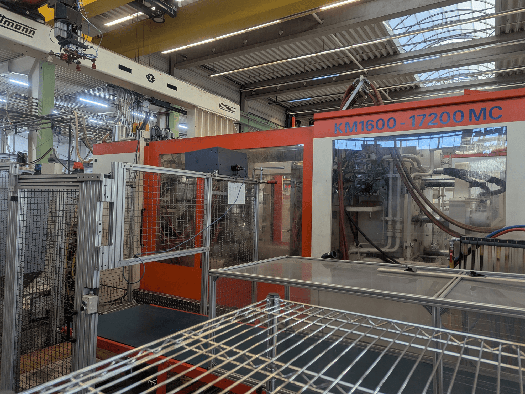 Máquina de moldagem por injeção hidráulica Krauss Maffei KM 1600-17200MC, vista frontal com painel de controlo visível e linhas hidráulicas.