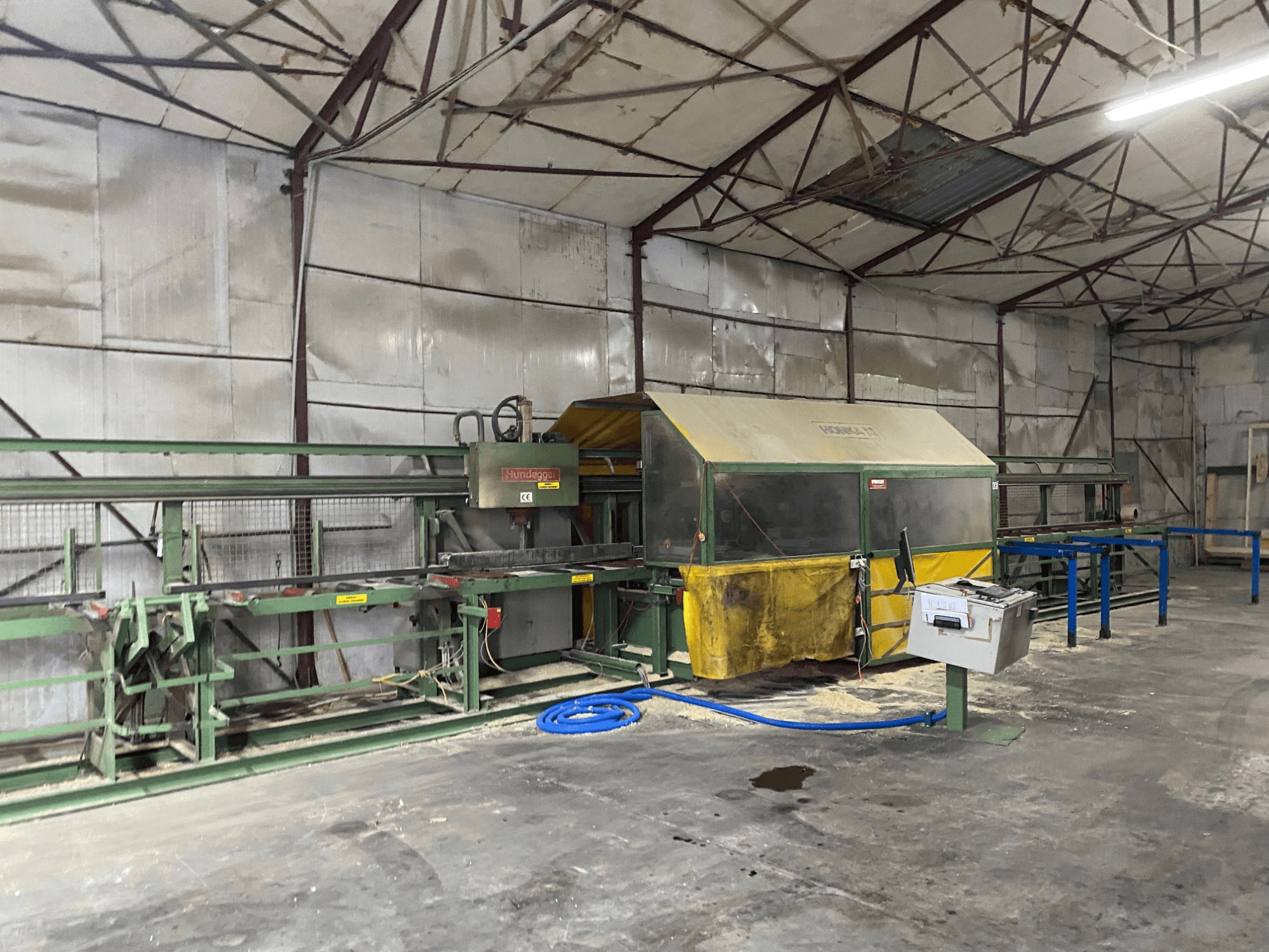 Centro de maquinação CNC para madeira HUNDEGGER K1 numa oficina, vista lateral mostrando máquinas, controlos e serradura no chão.