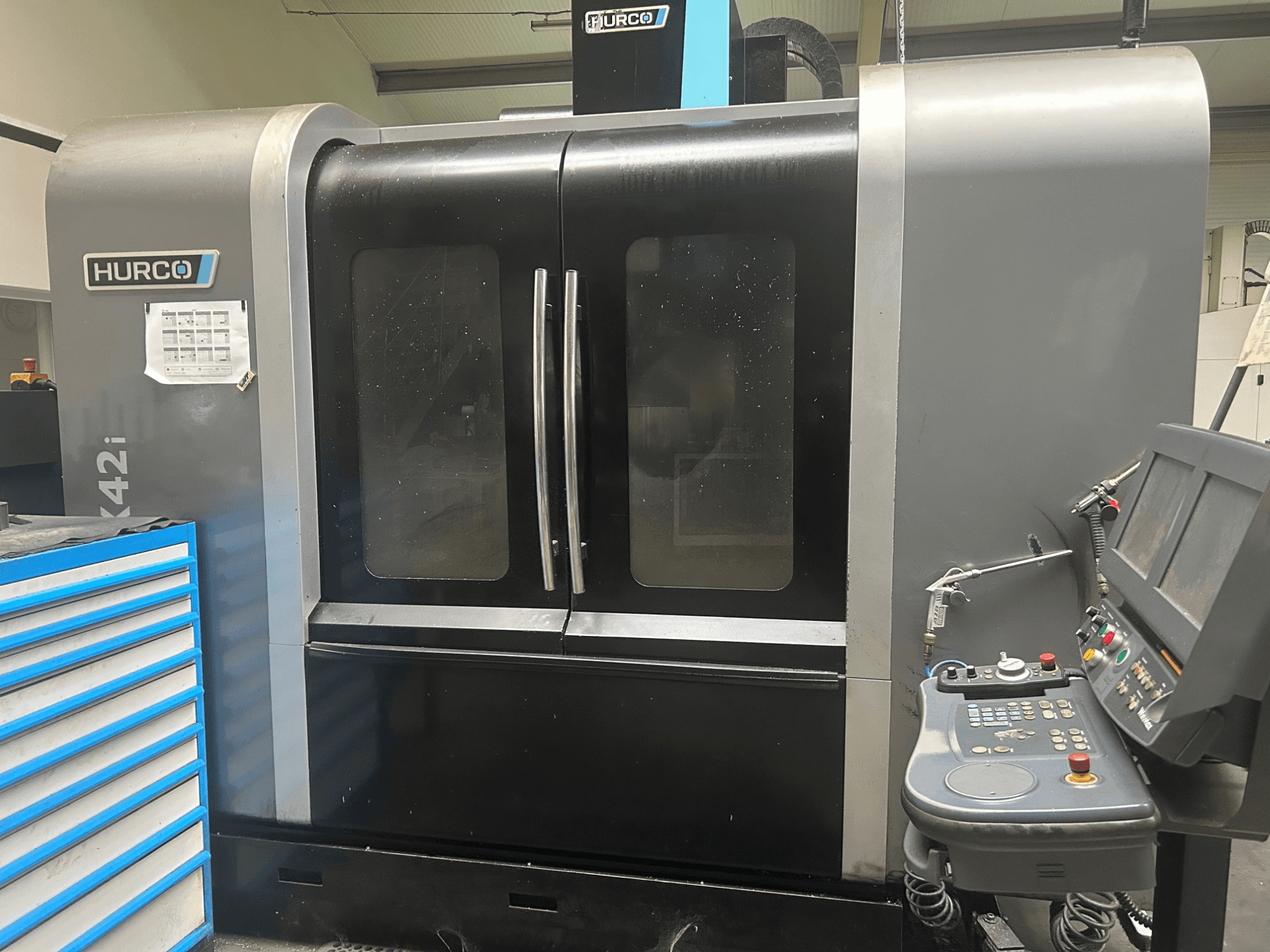 Máquina CNC Hurco VMX42i, vista frontal com painel de controlo lateral, com portas duplas e detalhes técnicos visíveis.