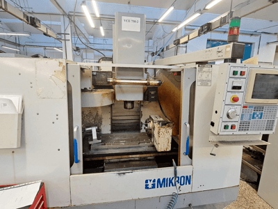 Fresadora CNC Mikron VCE 750-2, vista frontal, com painel de controlo e fuso na área de maquinagem, apresenta desgaste e sujidade.