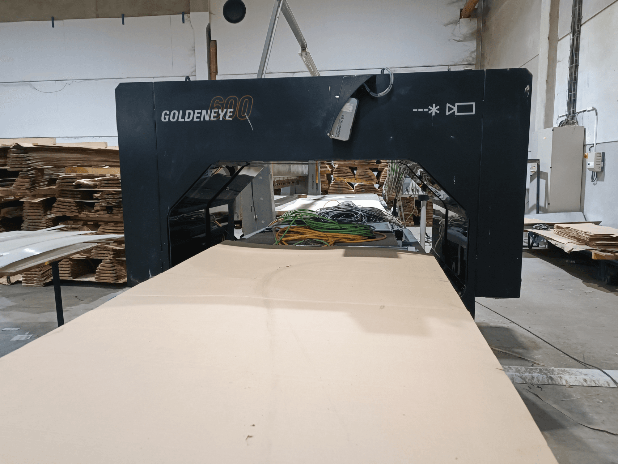 Vista frontal da máquina de processamento de madeira Microtec GOLDENEYE GLD 600 DSC, com grande superfície de corte e equipamento numa oficina.