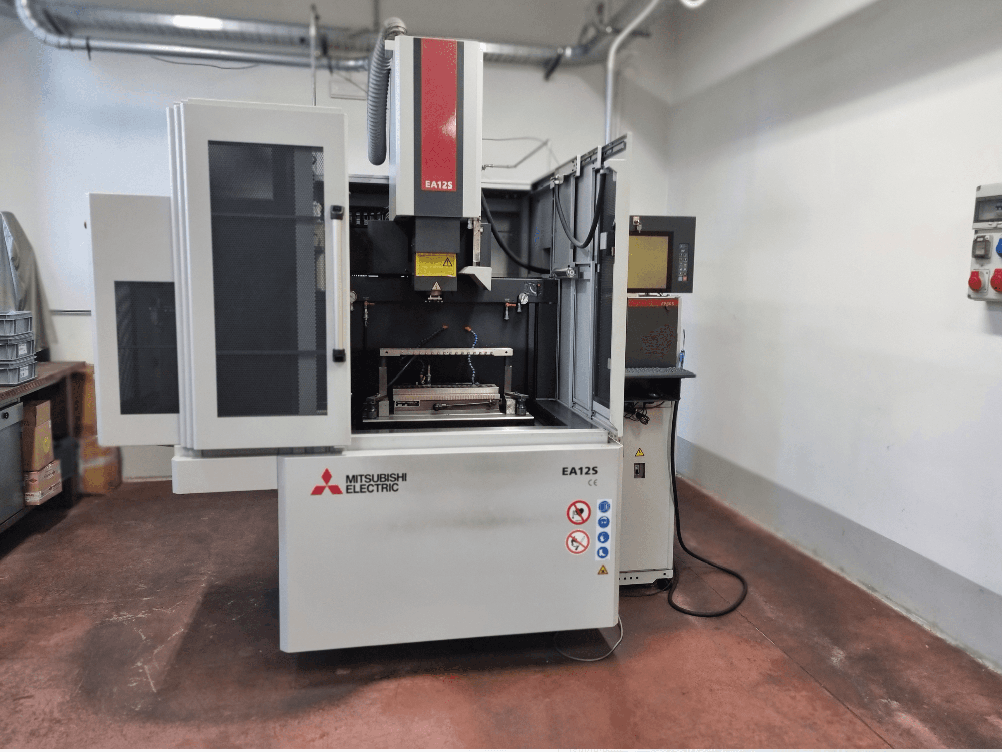 Máquina de corte de fio Mitsubishi Electric EA12S, vista frontal, com portas abertas, painel de controlo e etiquetas de segurança.