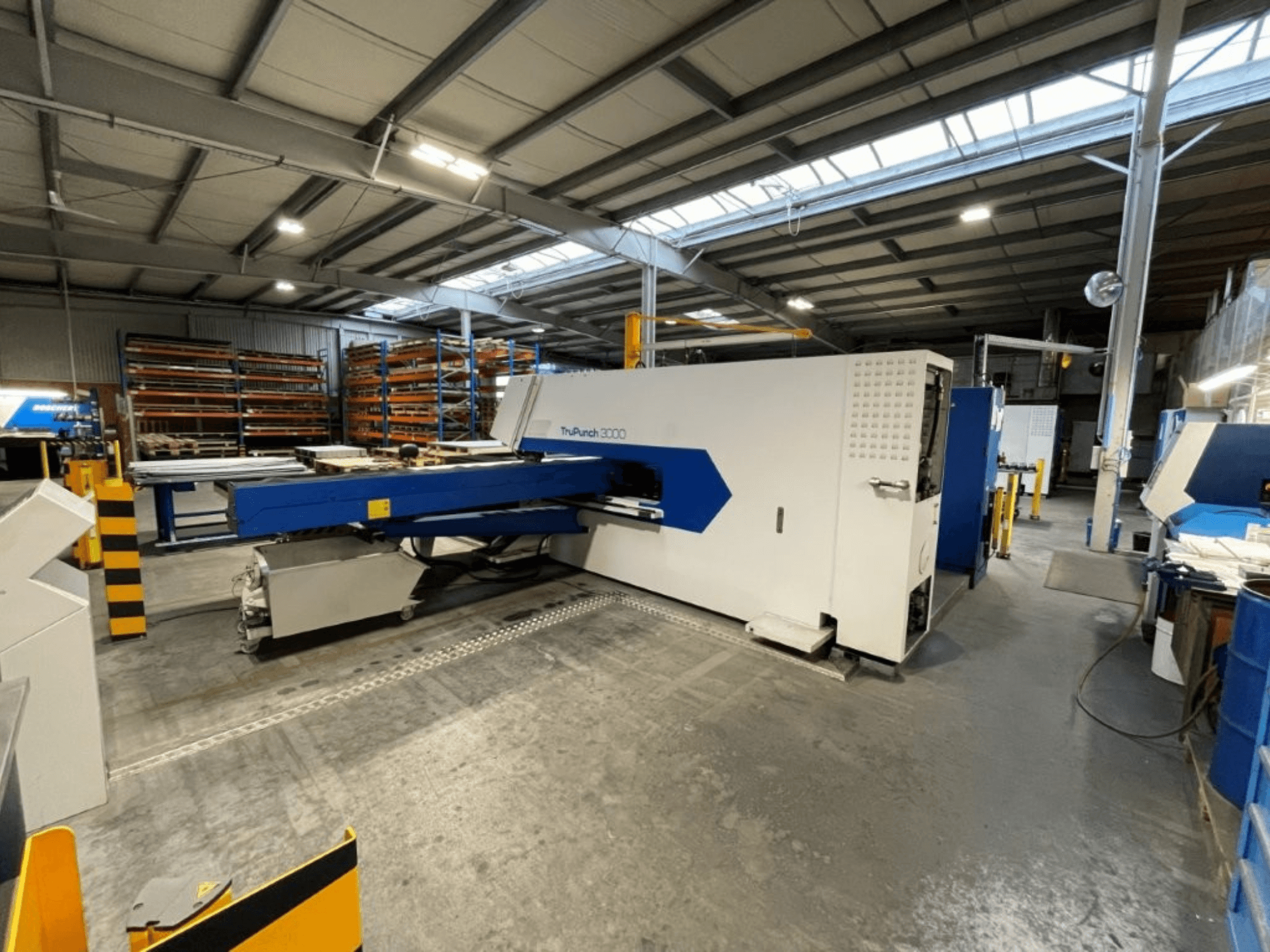 A prensa puncionadora CNC TRUMPF TruPunch 3000 num ambiente fabril; a vista frontal destaca o seu design azul e branco e os seus componentes operacionais.