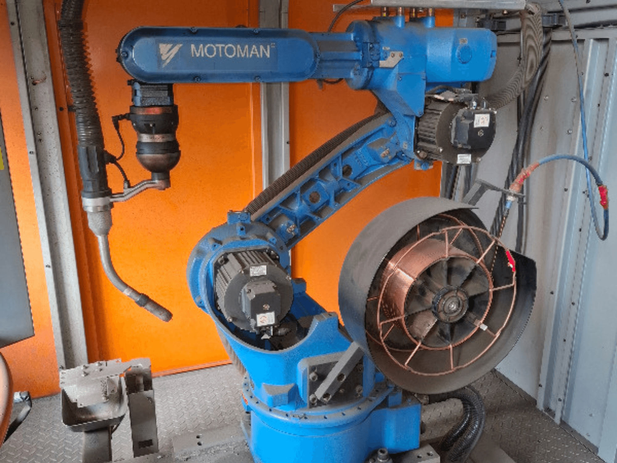 Braço robótico MOTOMAN em azul, vista lateral, com ventilador e ferramentas acopladas, mostrando detalhes mecânicos e ligações.