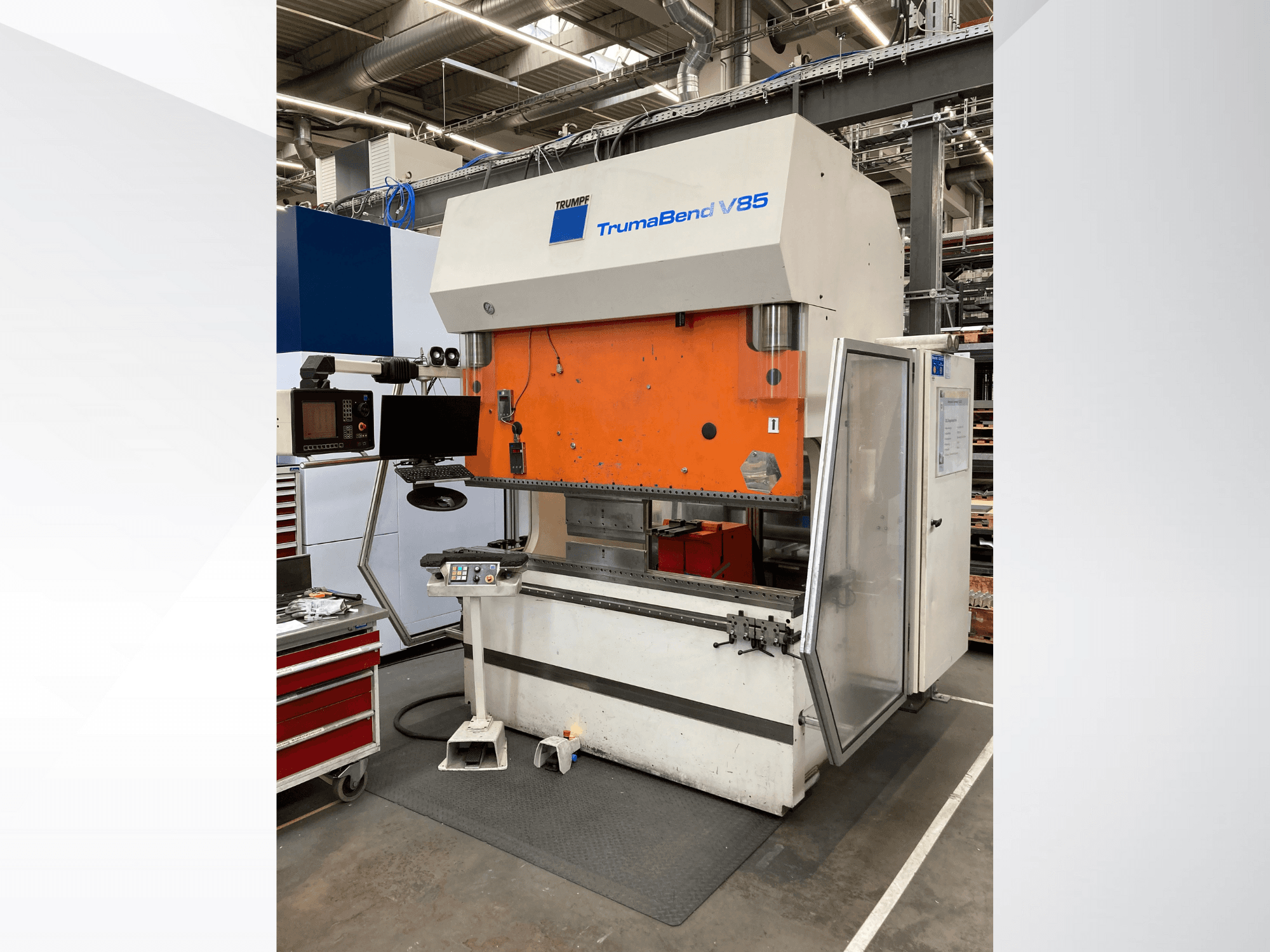 Máquina de dobragem TruMatic V85 numa fábrica, com painel frontal cor de laranja, ecrã de controlo e porta lateral aberta, vista lateral.