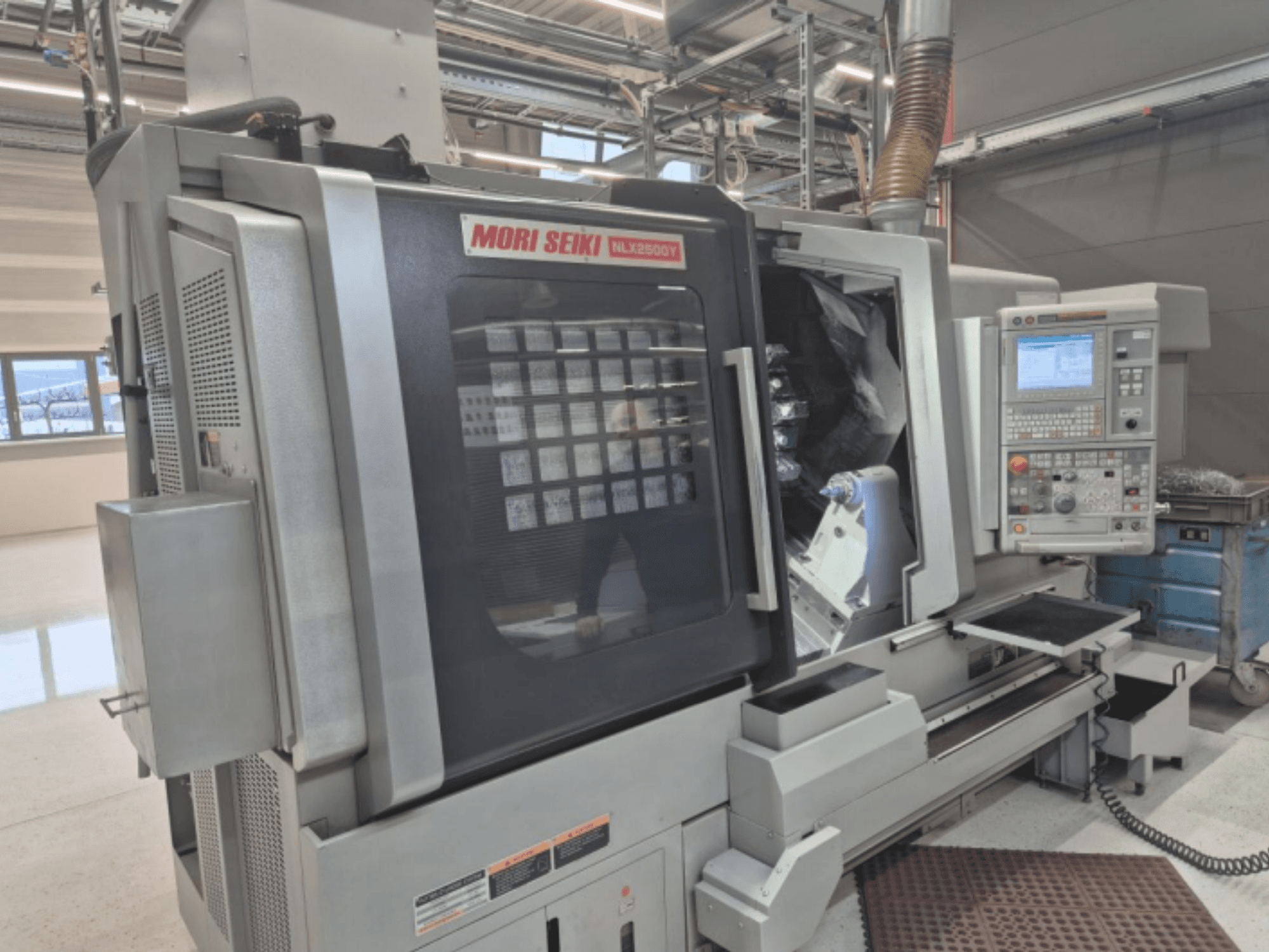 Torno CNC MORI SEIKI NL2500Y em fábrica, vista frontal do painel de controlo e da câmara da peça.