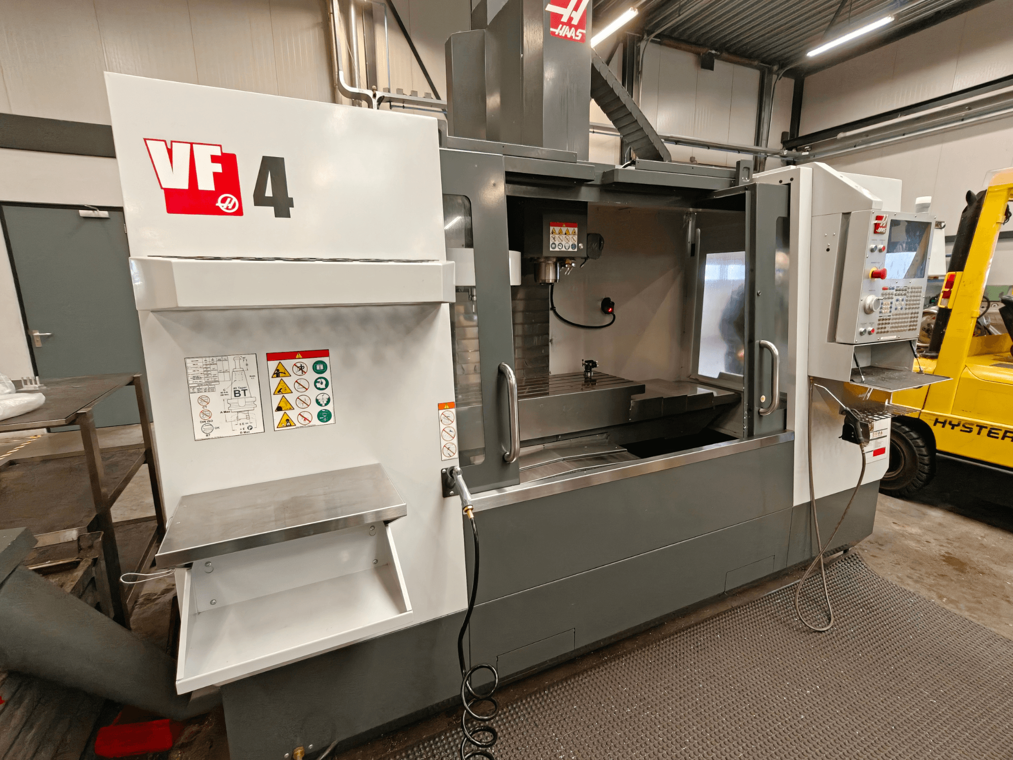 Centro de maquinação vertical HAAS VF-4, vista frontal, com painel de controlo, área de trabalho e etiquetas de segurança na lateral.