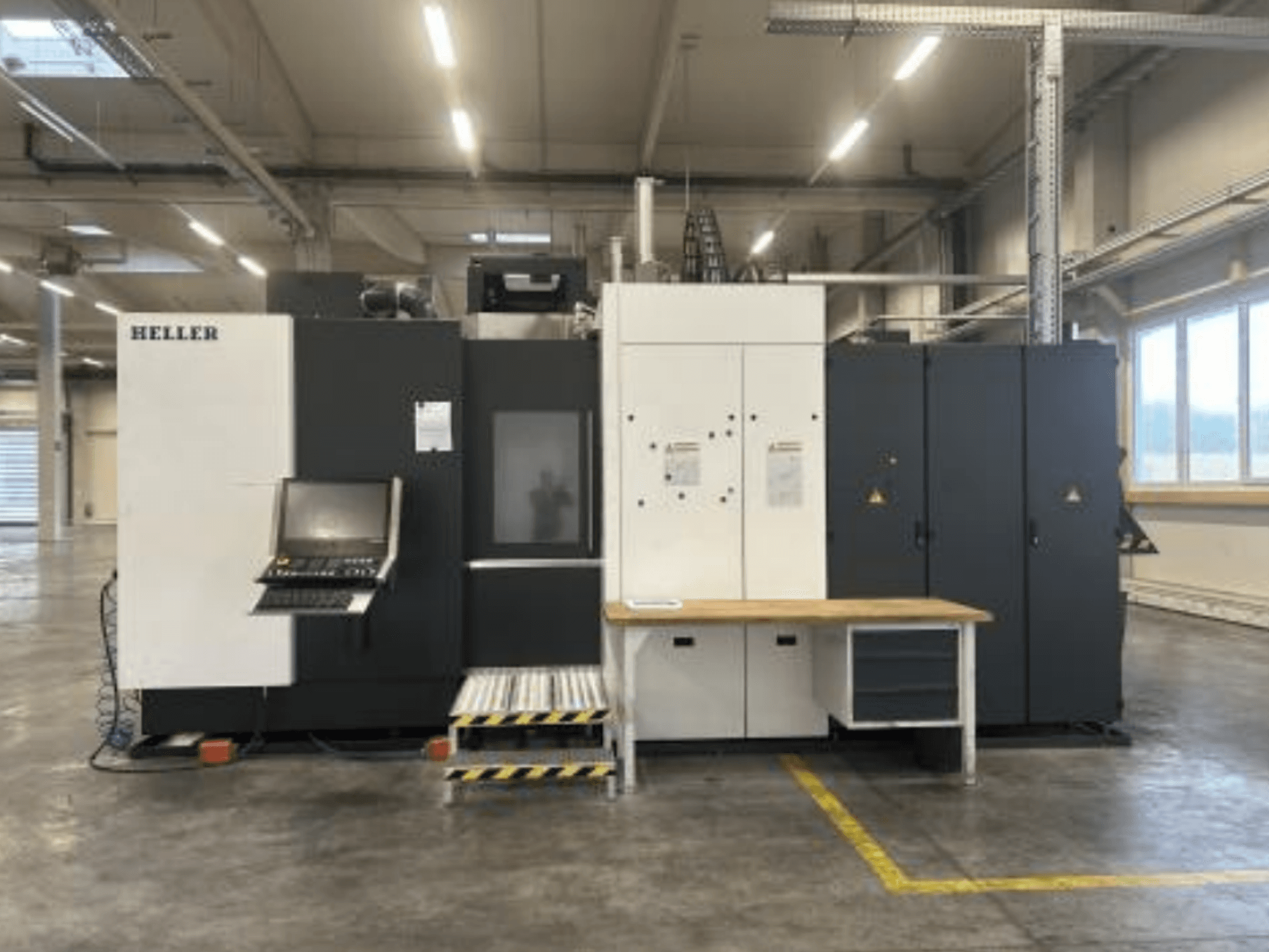Centro de maquinagem horizontal HELLER H5000, vista frontal que mostra o painel de controlo, o compartimento de armazenamento de ferramentas e a mesa de trabalho.