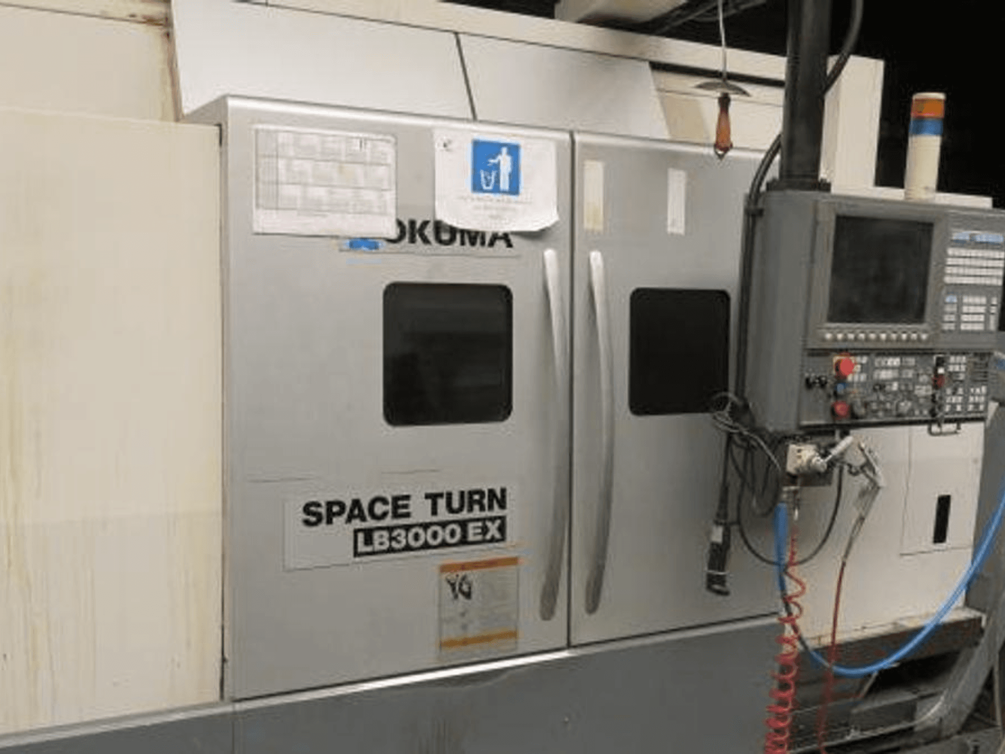 Torno CNC Okuma Space Turn LB3000 EX, vista lateral, com painel de controlo, duas portas e cablagem visível.