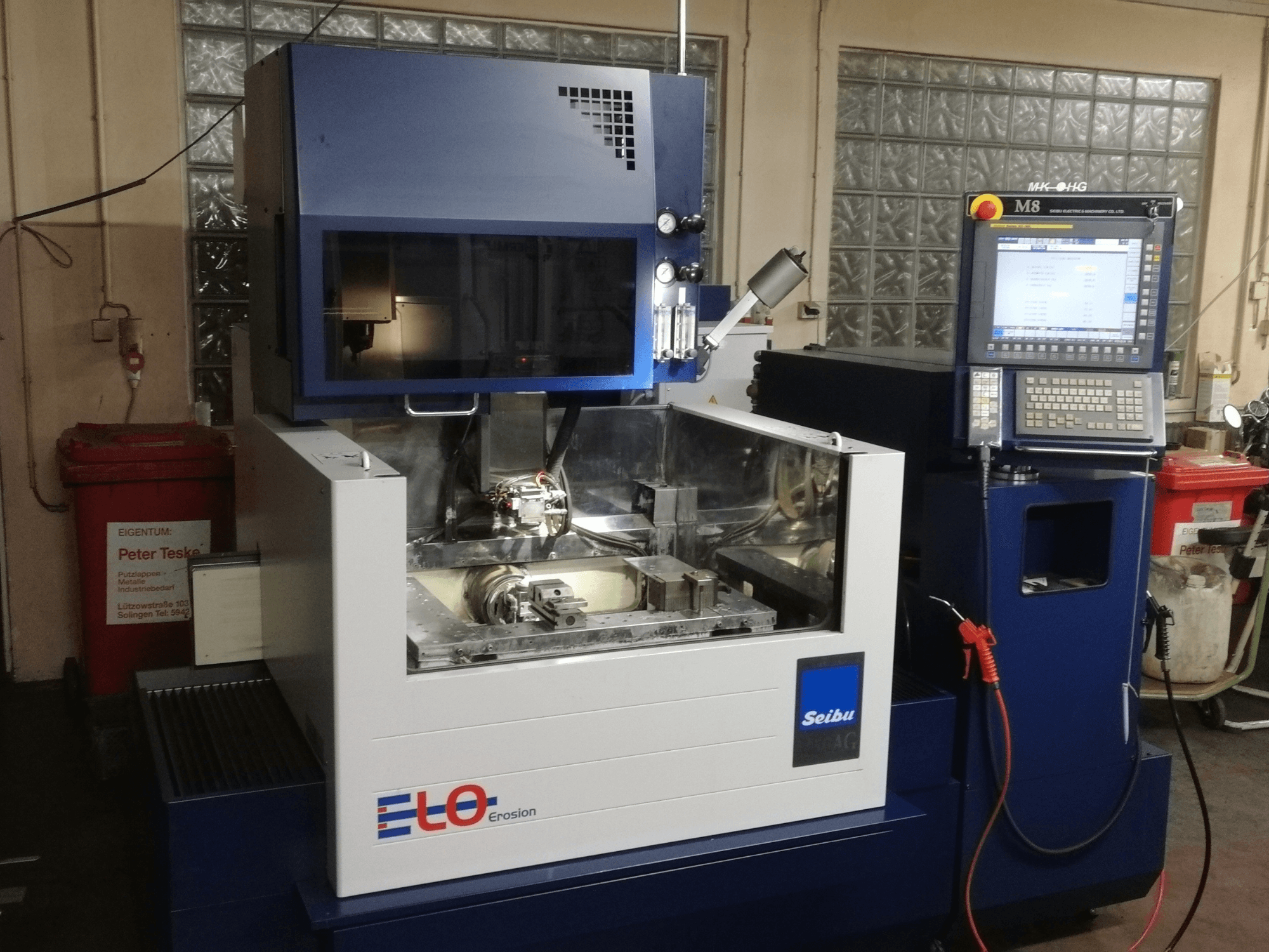 Máquina de erosão ELO Seibu vista de frente, com um painel de controlo e uma área de trabalho visível com componentes metálicos.
