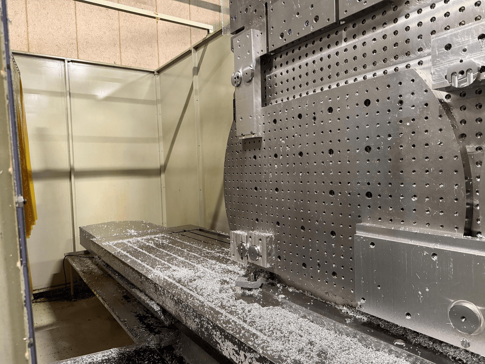 Vista frontal em grande plano do Centro de Maquinação Universal KIHEUNG KNC-U1000, mostrando uma mesa de trabalho em metal com aparas de alumínio.